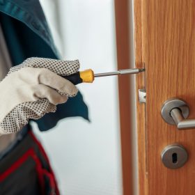 Close up of locksmith workman in uniform installing door knob. Professional repair service